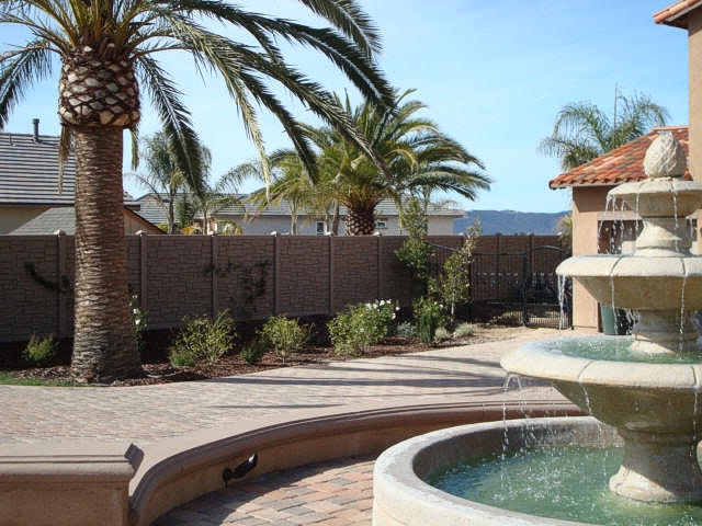 a backyard with a vinyl fence, water fountain and palm trees