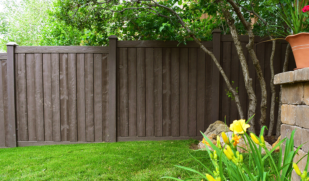 Brown vinyl wood fence with a tree’s branches hanging over the top