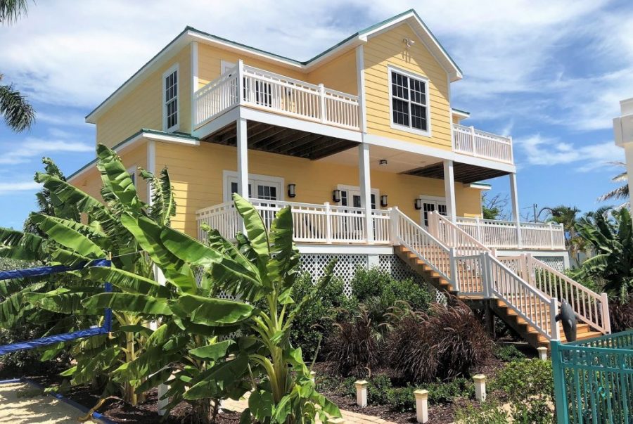  Yellow two-story home with white railings surrounding the deck, patio and staircase