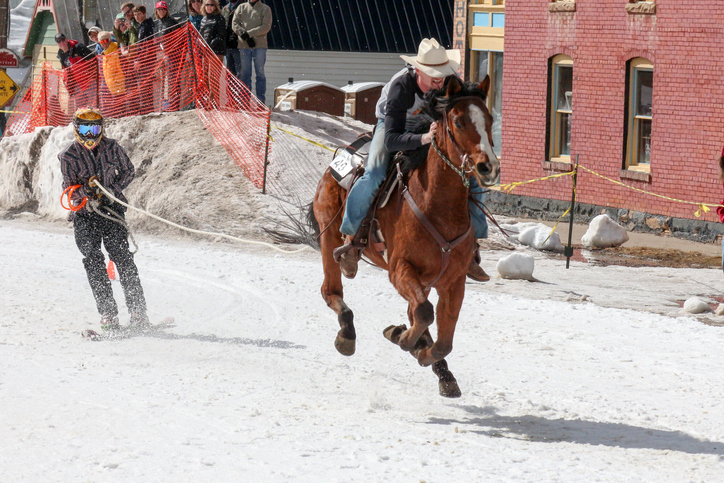 Skijoring event with a person riding a horse pulling a skier across snow